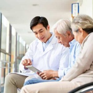 young asian doctor discussing test result and diagnosis with senior couple patients using digital tablet in hospital hallway